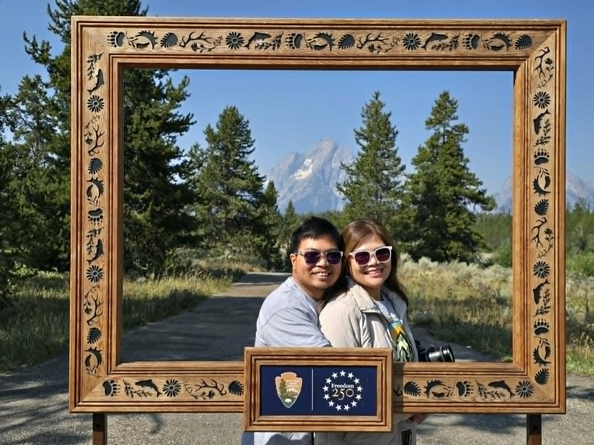 Rochelle and Nathaniel posing inside a wooden picture frame with the Teton range behind them